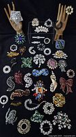Overall lot of 38 brooches arranged on black background with wooden display hands