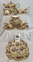 Full display of 16-piece Royal Winton vintage chintz china set with teapot, gravy boat, cups, saucers, and plates arranged on a white draped background