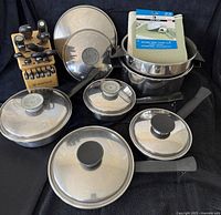 Overview of knife block set, cookware pieces and drying mat arranged on black cloth