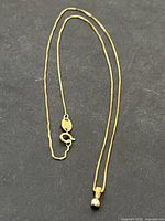 Close-up image of fine yellow gold chain necklace with spring ring clasp and attached pendant.
