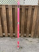 Full view of the 6 foot pink aluminum level leaning against a wooden fence, showing overall condition including paint wear.