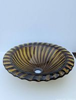 Bronze ribbed glass vessel sink or bird bath, angled view showing scalloped rim and striped pattern, with central drainage hole.