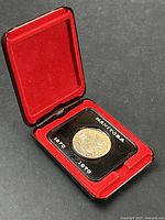 Red display case lined with red velvet containing the Manitoba commemorative silver dollar coin dated 1870-1970.