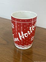 Front and side view of Tim Hortons holiday-themed ceramic mug showing red and white winter sweater pattern with snowflakes and Christmas trees.