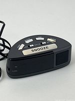 Close-up of front and top of black digital alarm clock showing large silver snooze button and function buttons