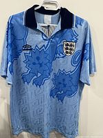 Front of the England light blue soccer jersey by Umbro with detailed lion design and team crest