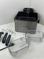 Hamilton Beach stainless steel deep fryer with two wire mesh baskets and four skewers displayed on white background.