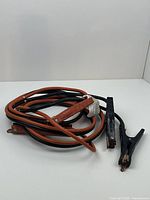 Photo of coiled heavy duty jumper cables with red and black insulation and metal clamps with plastic covers.