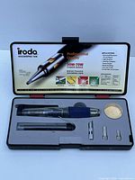 Top view of the open Iroda Solderpro 50k soldering iron kit showing the main soldering tool with blue grip, multiple metal tips, brass sponge cleaner, and inside of the case lid with printed product details.