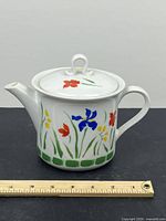 Front view of the Japanese porcelain floral teapot with a ruler for scale, showing red, blue, and yellow flowers with green leaves on a white base.