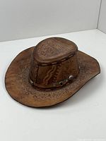 Photo of the brown leather cowboy hat showing the hand-tooled floral and western designs on the crown and brim and metal stud accents on leather band.