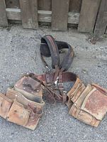 Full view of the worn leather tool belt with attached shoulder harness strap resting on ground.