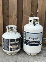 Photo showing the two Bernzomatic propane tanks side by side outside, smaller and larger sizes visible, both white metal with visible labels.