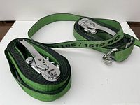 Two green ratchet tie down straps laid flat showing ratchet mechanisms and metal hooks.