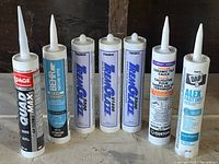 Seven tubes of various caulking and sealing products arranged horizontally, showing front labels clearly.