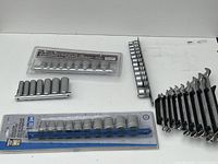 Various socket wrench heads on rails and set of combination wrenches laid out on white surface.