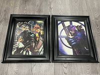 Two framed superhero pictures side by side on wooden floor: left features Black Panther with another character on rooftop, right features Hawkeye aiming bow.