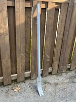 Full view of the 57-inch heavy duty pry bar leaning against a wooden fence. The pry bar is painted light gray and appears sturdy.