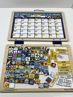 Full view of the open wooden calendar showing the monthly grid with magnetic date numbers attached on the top and a large number of colorful event tiles below them arrayed on the bottom panel.