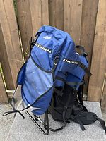 Side view of blue child carrier hiking backpack showing metal frame, mesh pocket, and padded straps.