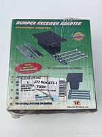 Front view of the sealed green and white box with images of the bumper receiver adapter and mounting screws counted as part of the accessory kit, including product and brand information.