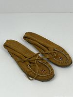 Pair of brown low leather moccasins viewed from the top and side, showing stitching and lace ties.