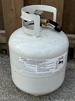 Full view of the white propane tank showing valve with attached black hose and metal protective collar.