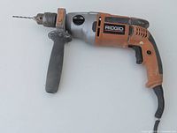 Front angled view of the Ridgid R5011 hammer drill with side handle and drill bit attached, showing the drill's body, grip, and general condition.