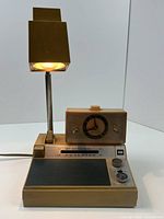 Vintage beige ROSS RE-83 clock radio with clear analog clock face, AM/FM radio controls, and telescoping lamp turned on.