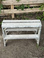 Front view of short wooden construction bench/step stool showing paint splatter and foldable leg support.