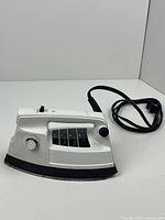 Front and side angled view of white electric iron with black soleplate, power cord coiled nearby
