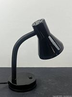Photo of the small black desk lamp standing upright on a flat surface, showing the flexible neck and bell-shaped lamp head.
