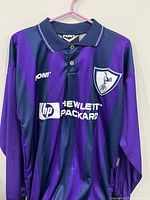 Front view of a long-sleeve soccer jersey with vertical purple and navy stripes, Pony logo on chest, Hewlett Packard logo center, and embroidered team crest with cockerel and soccer ball.