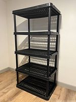 Complete assembled shelving unit with four tiers of black plastic shelves and vertical poles
