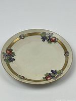 Top view of vintage ceramic decorative plate with fruit motifs and gold border, showing condition and design details.