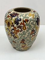 Side view of oval-shaped ceramic vase with abstract floral and geometric patterns in multi-color and gold accents.