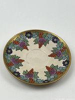 Top view showing floral design with purple, lavender, orange, and blue flowers with green leaves and gold rim.