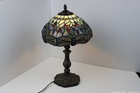 Photo of the lamp fully assembled with stained glass dragonfly shade illuminated showing colorful details and ornate metal base.