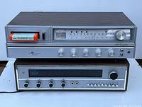 Front and top angle view showing tuner unit with analog tuning meter and cassette deck and amplifier unit below with control knobs and black tuning display.