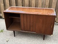 Front left angled view of vintage wooden buffet showing sliding doors open to reveal shelving space on the left side, surface wear on top, and overall structure.