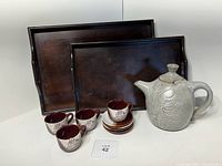 Full set showing two dark wood trays, beige ceramic teapot, four matching mugs and four saucers