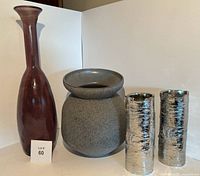 Four decorative vases shown together: tall burgundy glass vase, short wide-mouth grey ceramic vase, two metallic silver-toned textured vases