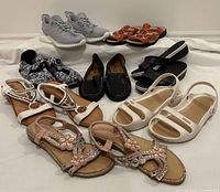 All 10 pairs of assorted women's footwear displayed together showing variety of styles and colors including sandals, loafers, flats and runners.