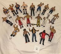 Photo of twenty WWE wrestling action figures arranged on a white surface, showing a variety of wrestlers in different poses and costumes.