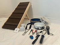 Full view of the pet ramp, three ceramic dog bowls, two white plastic food/water dispensers, slip leash, metal training collar, and various grooming tools including brushes, comb, de-shedding blade, nail clippers, nail file, grooming scissors, training clicker, and flea comb.