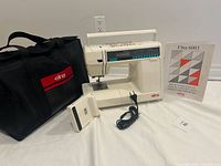 Machine, case, foot pedal, power cord, manual and accessories arranged on white surface