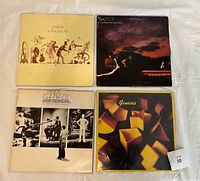 Four Genesis vinyl LP albums laid flat showing front covers from A Trick of the Tail, ...And Then There Were Three..., The Lamb Lies Down on Broadway, and Genesis (1983).