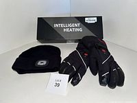 Pair of new black heated gloves with touchscreen fingers and reflective details, black LED beanie, and the gloves' box with 'Intelligent Heating' branding