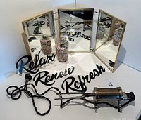 Photo of all lot items arranged: vintage electric curling iron, brass tri-fold vanity mirror, two floral vases, and three black metal wall signs.