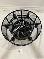 Top view of matte black flush mount ceiling fan with enclosed blades and mesh cage, showing wiring and structural arms.
